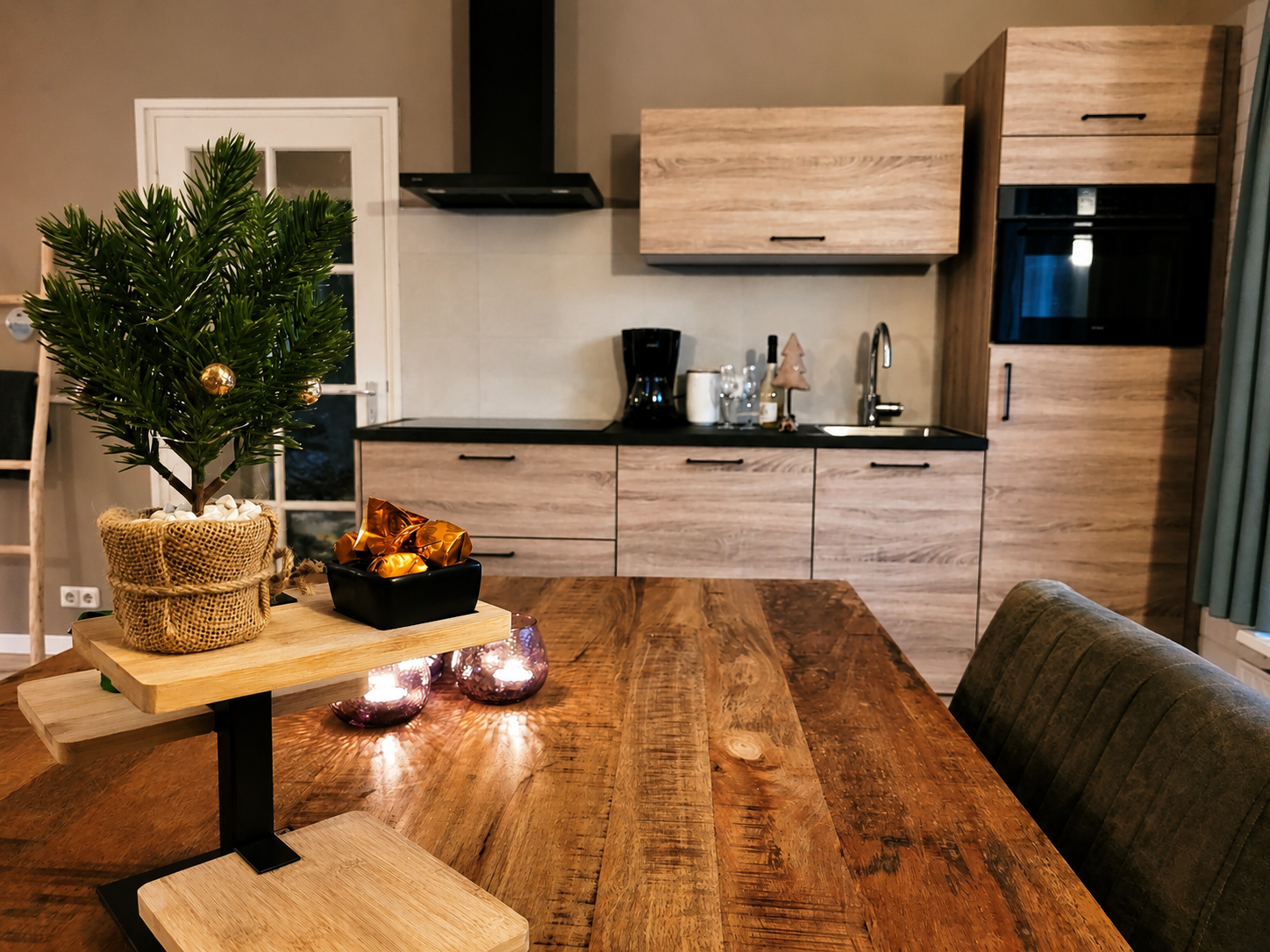 Moderne keuken met houten kastjes, eettafel en een klein, versierd boompje in een pot als middelpunt.