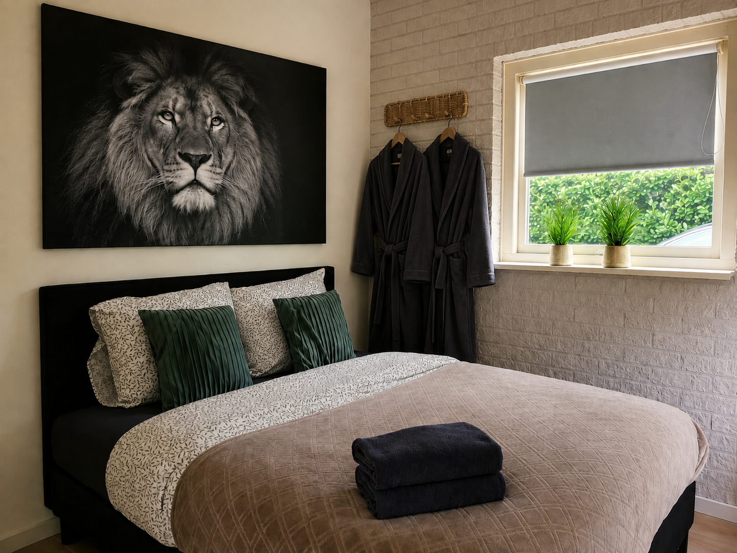 Moderne slaapkamer met muurdecoratie van een leeuw, een zwart bed, opgevouwen handdoeken en een raam met planten.