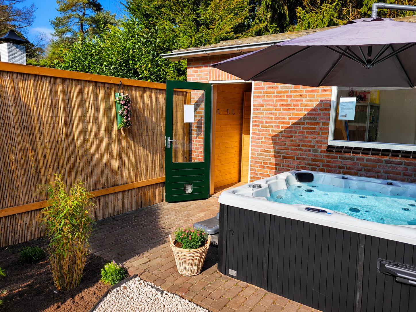 Terras in de achtertuin met jacuzzi, bakstenen muur, groene poort en parasol in de zon.