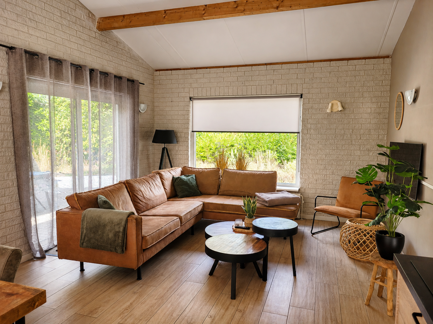 Lichte woonkamer met beige hoekbank, houten vloer, grote ramen en moderne inrichting.