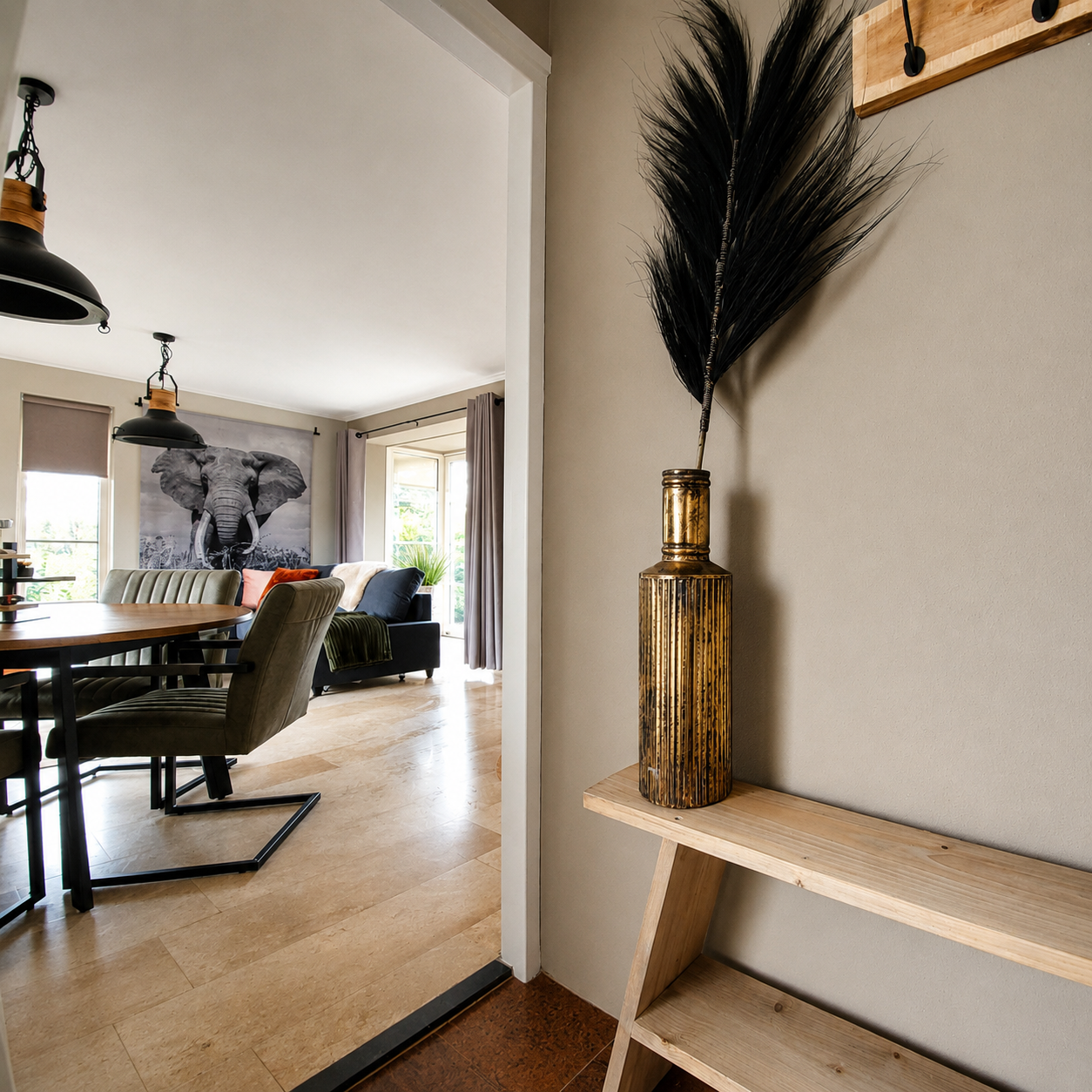 Moderne entree met een houten bank, gouden vaas en decoratie met veren, die uitkomt op een lichte eetkamer.