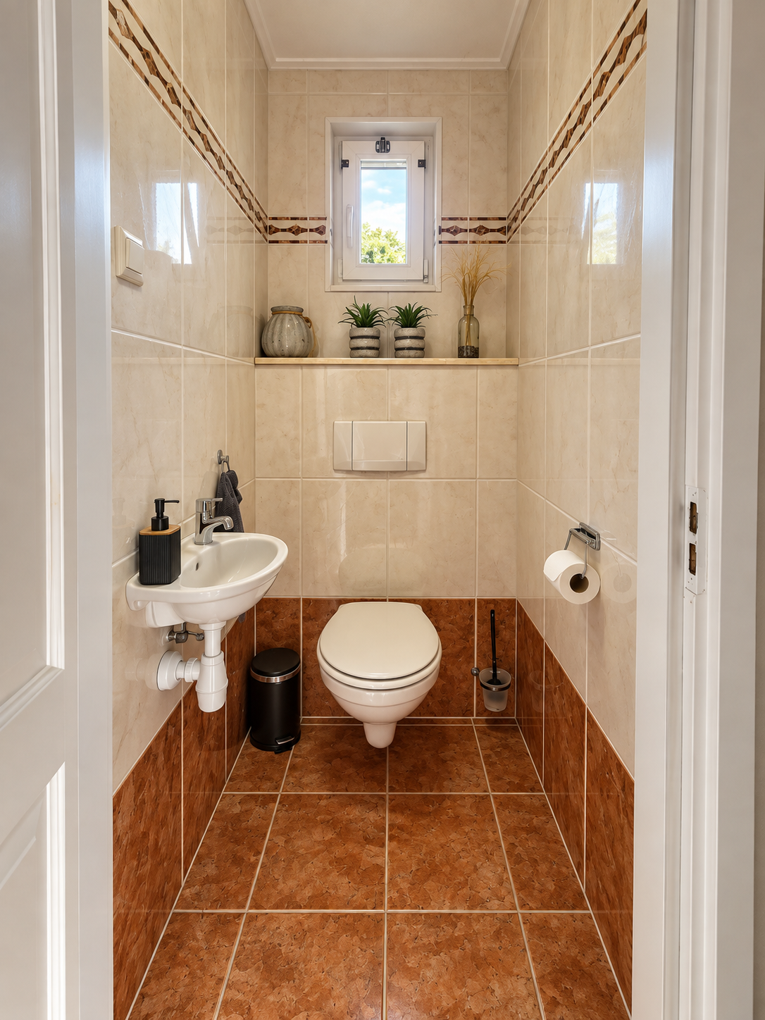 Smalle, betegelde badkamer met toilet, kleine wastafel en vensterbank met planten.