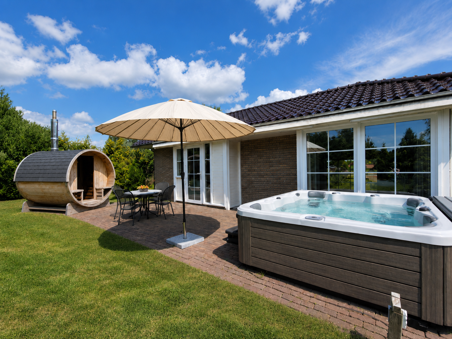 Terras in de achtertuin met een jacuzzi, parasol, ligstoelen en een barrelsauna naast een huis.