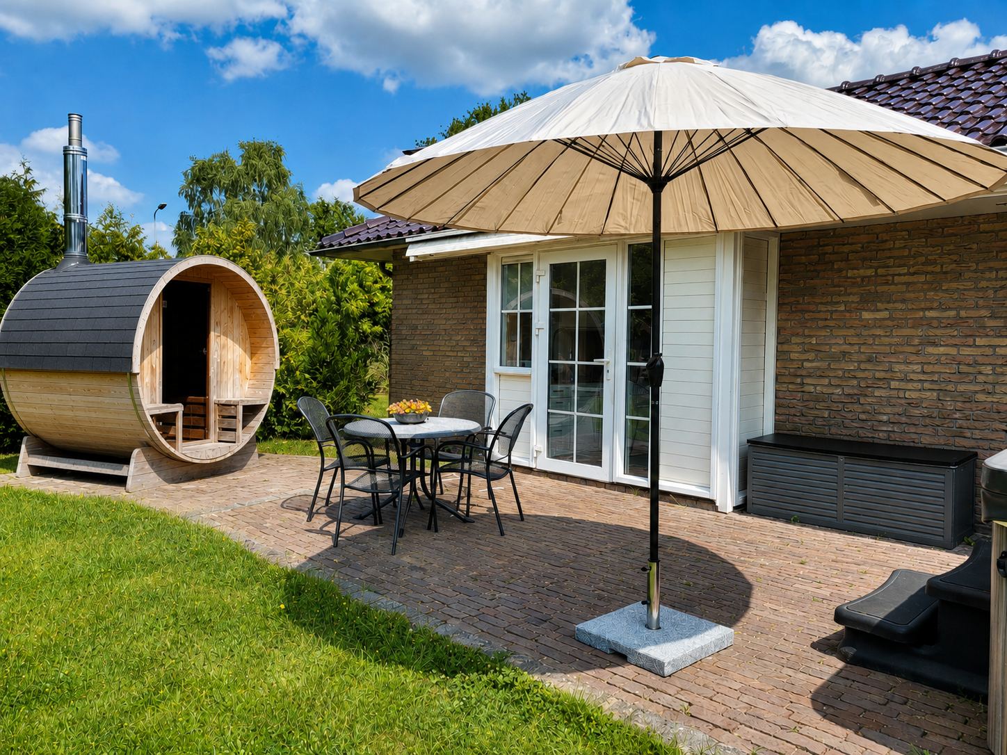 Terras in de achtertuin met een grote parasol, tafel en stoelen, een houten saunaton en een gazon onder een blauwe hemel.