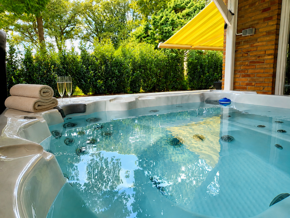 Jacuzzi in de achtertuin met helder water, een stenen rand, opgevouwen handdoeken en een geel zonnescherm, omgeven door groen.