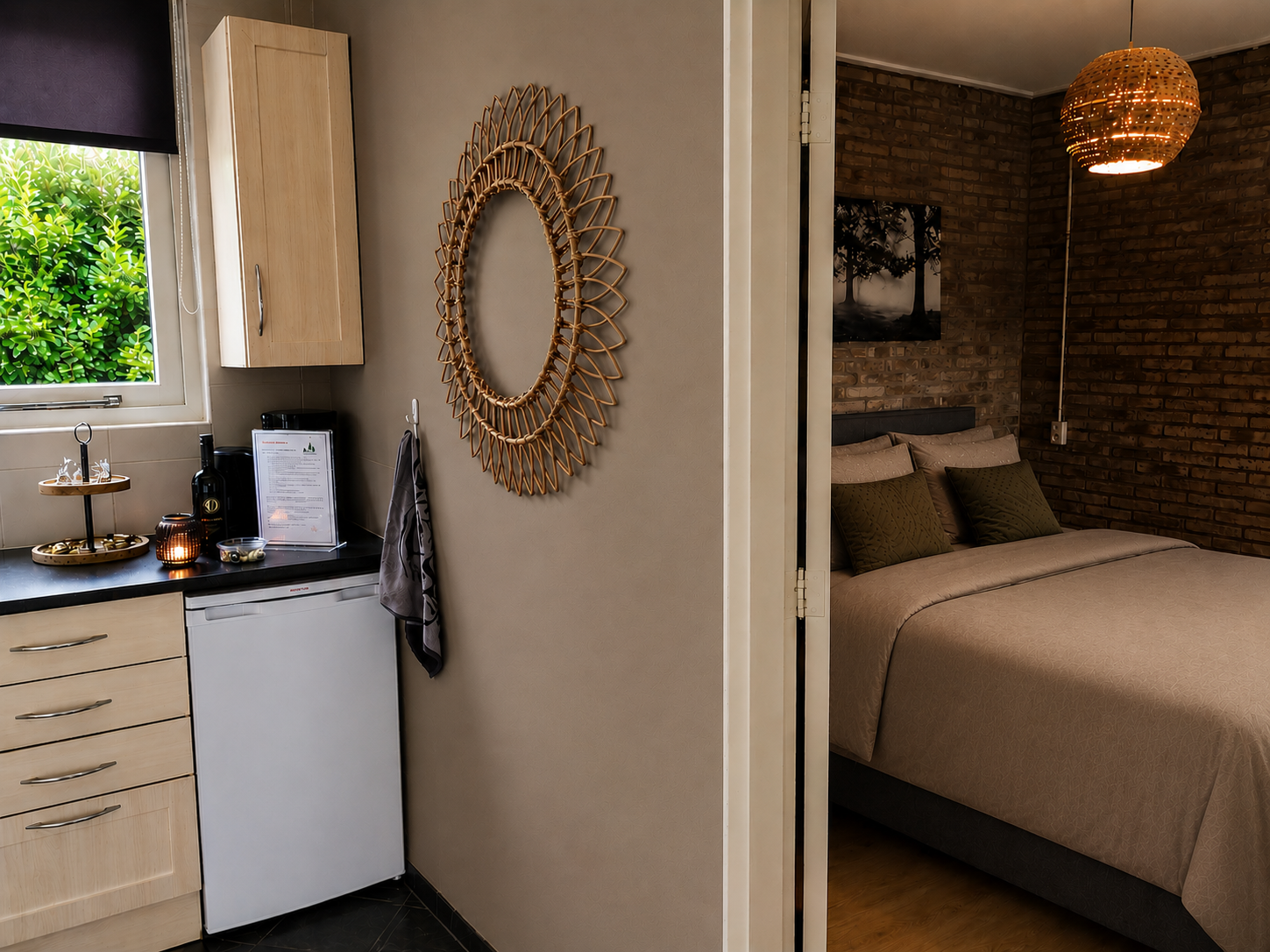 Compacte slaapkamer met beige muren, rieten spiegel, kitchenette en een open doorgang naar een bed in een kamer met bakstenen accenten.
