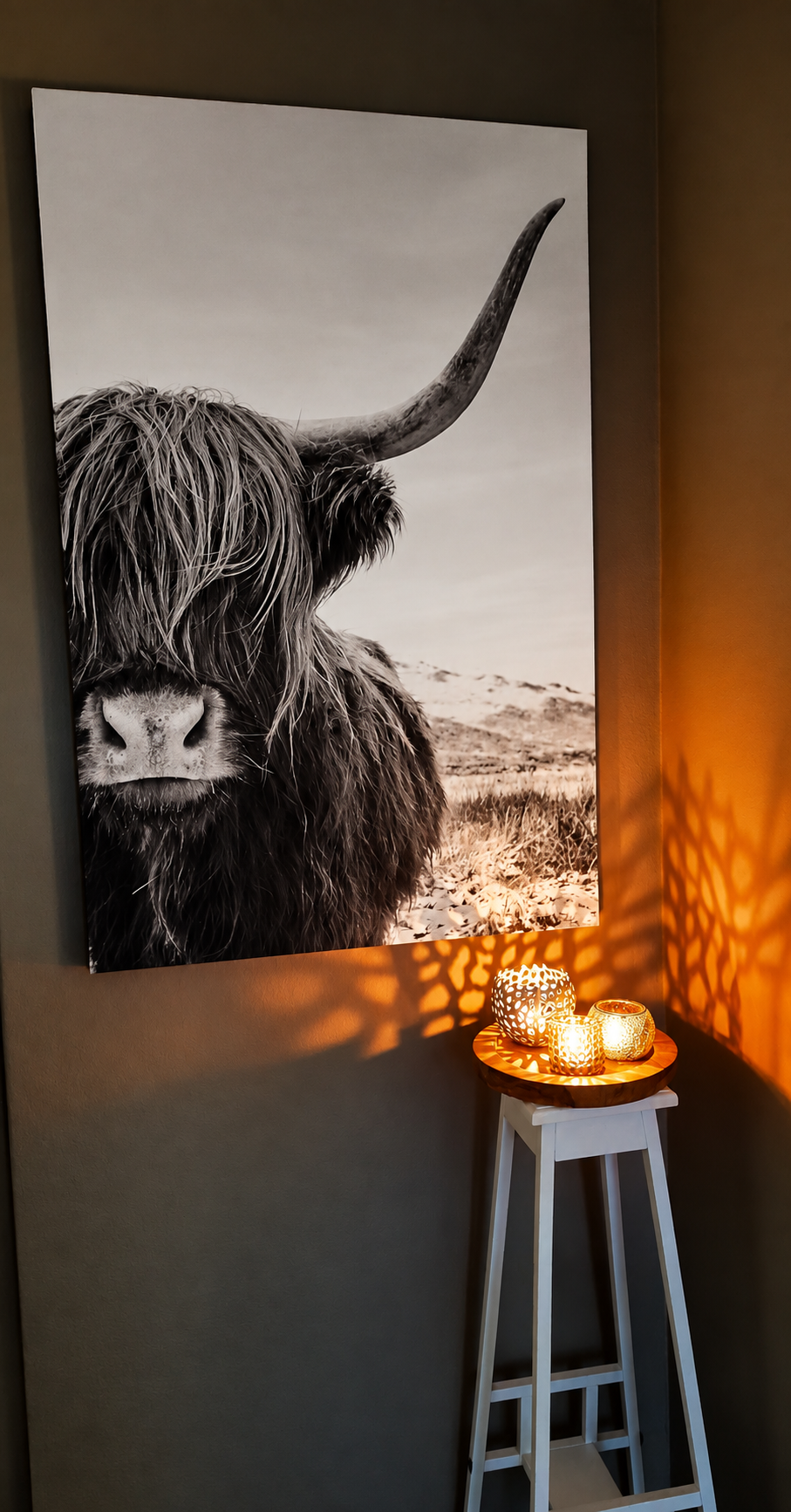 Zwart-wit schilderij van een ruige Schotse hooglandkoe boven een brandende kaars op een krukje in een schemerige hoek.