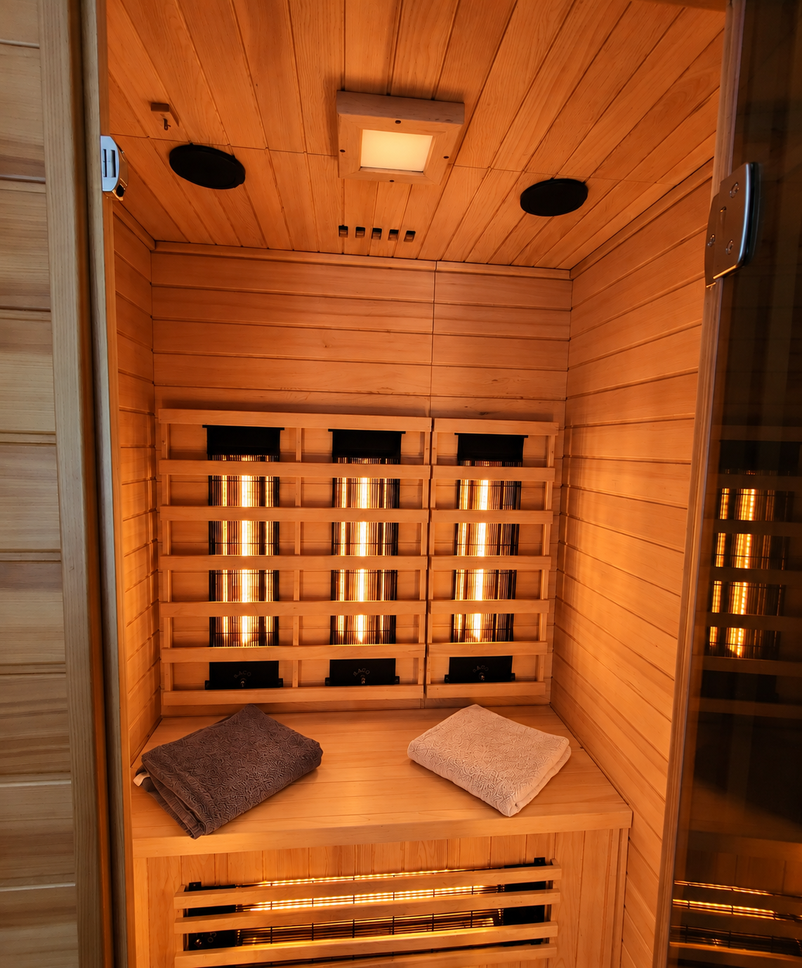 Sauna met houten lambrisering, gloeiende kachels en twee kussens op een bankje binnenin.