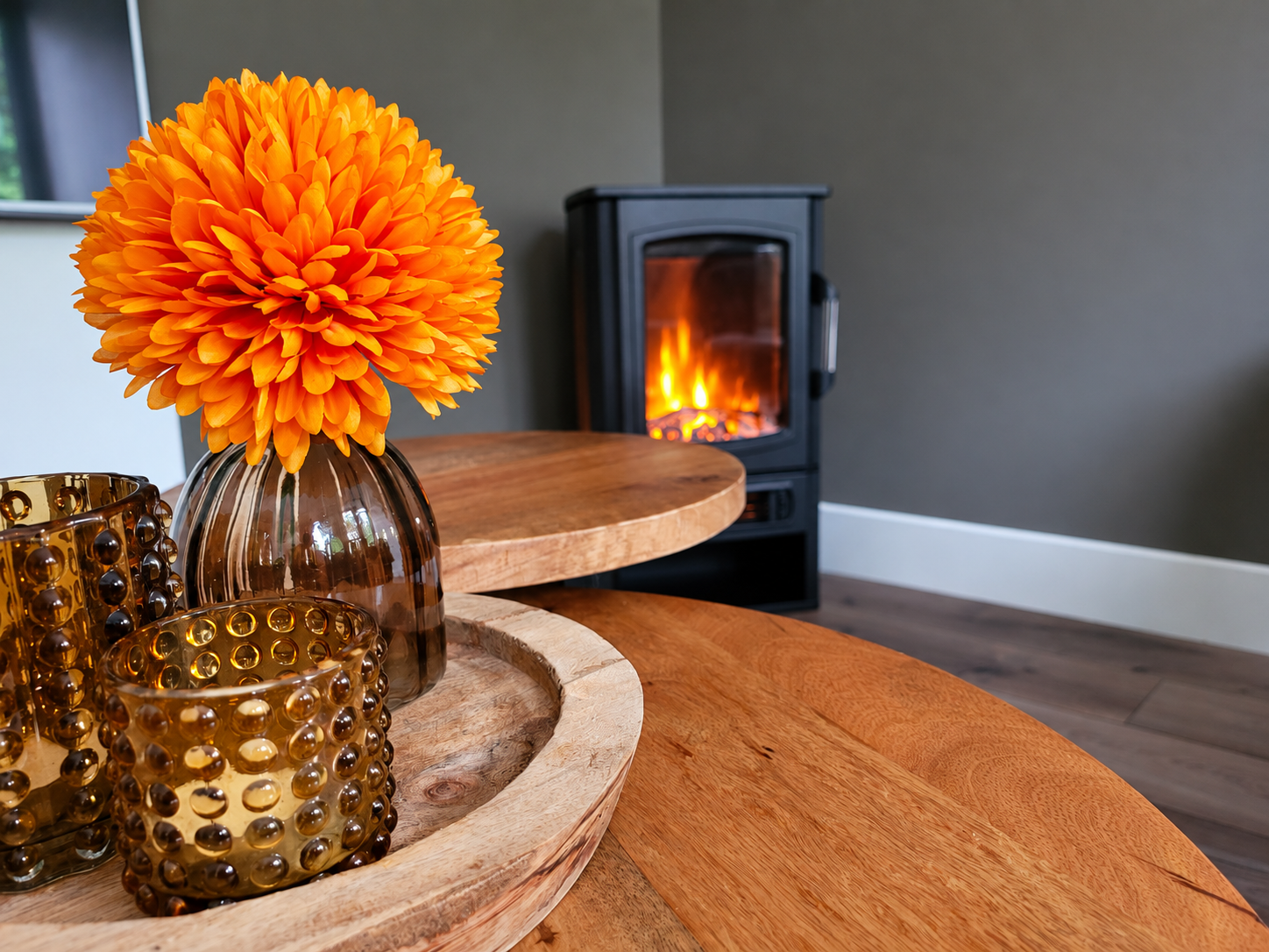 Woonkamer met een feloranje bloemstuk en kaarsen naast een brandende open haard.