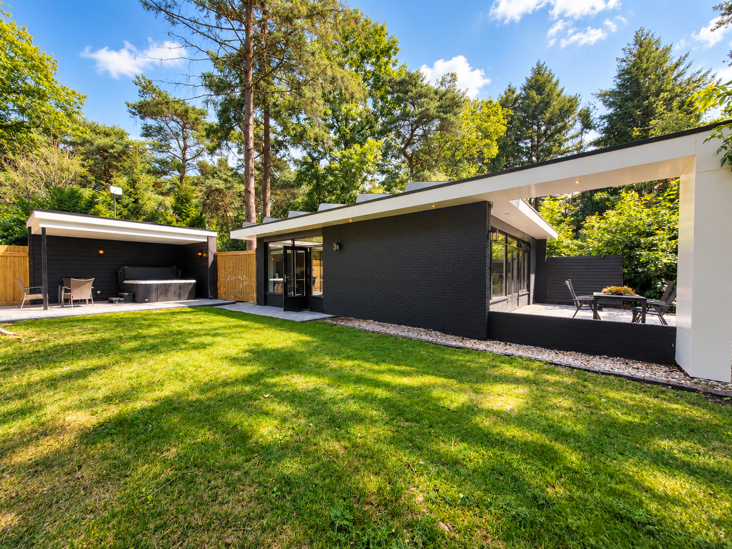 Moderne woning met een donkere buitenkant, grote open patio's en een zonnig groen gazon omgeven door bomen.