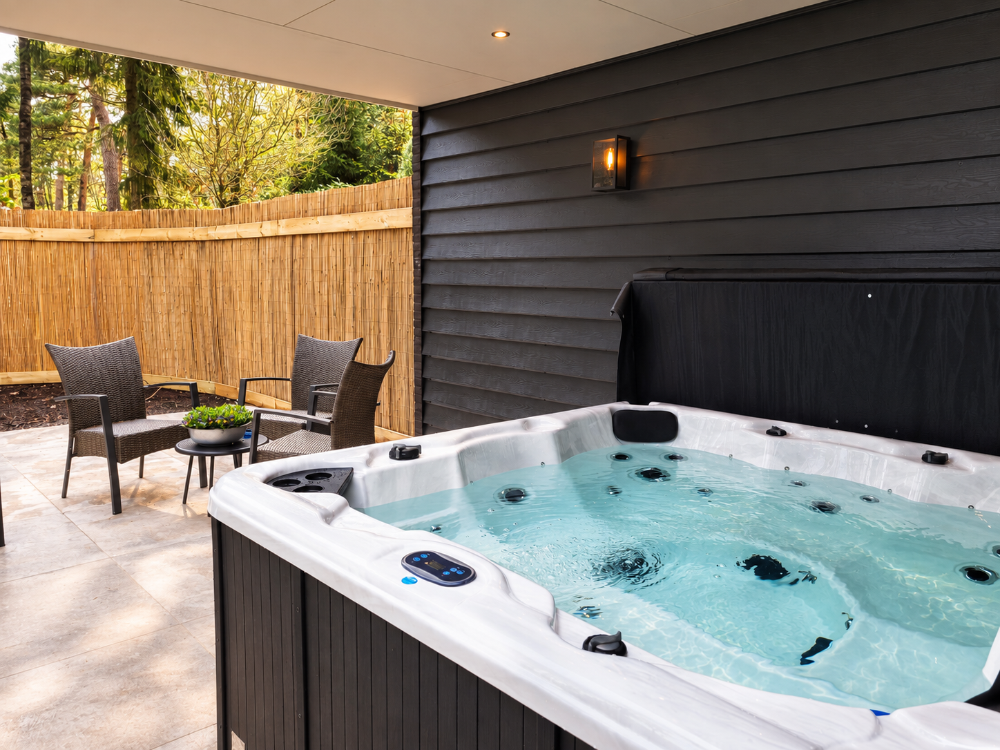 Terras in de achtertuin met een jacuzzi, tuinmeubilair en een schutting voor extra privacy bij zonsondergang.