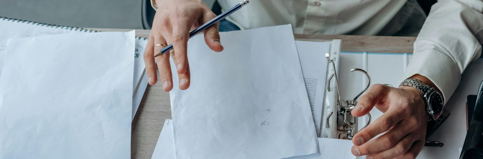 Hands holding a pen, reviewing papers on a desk; close-up view.