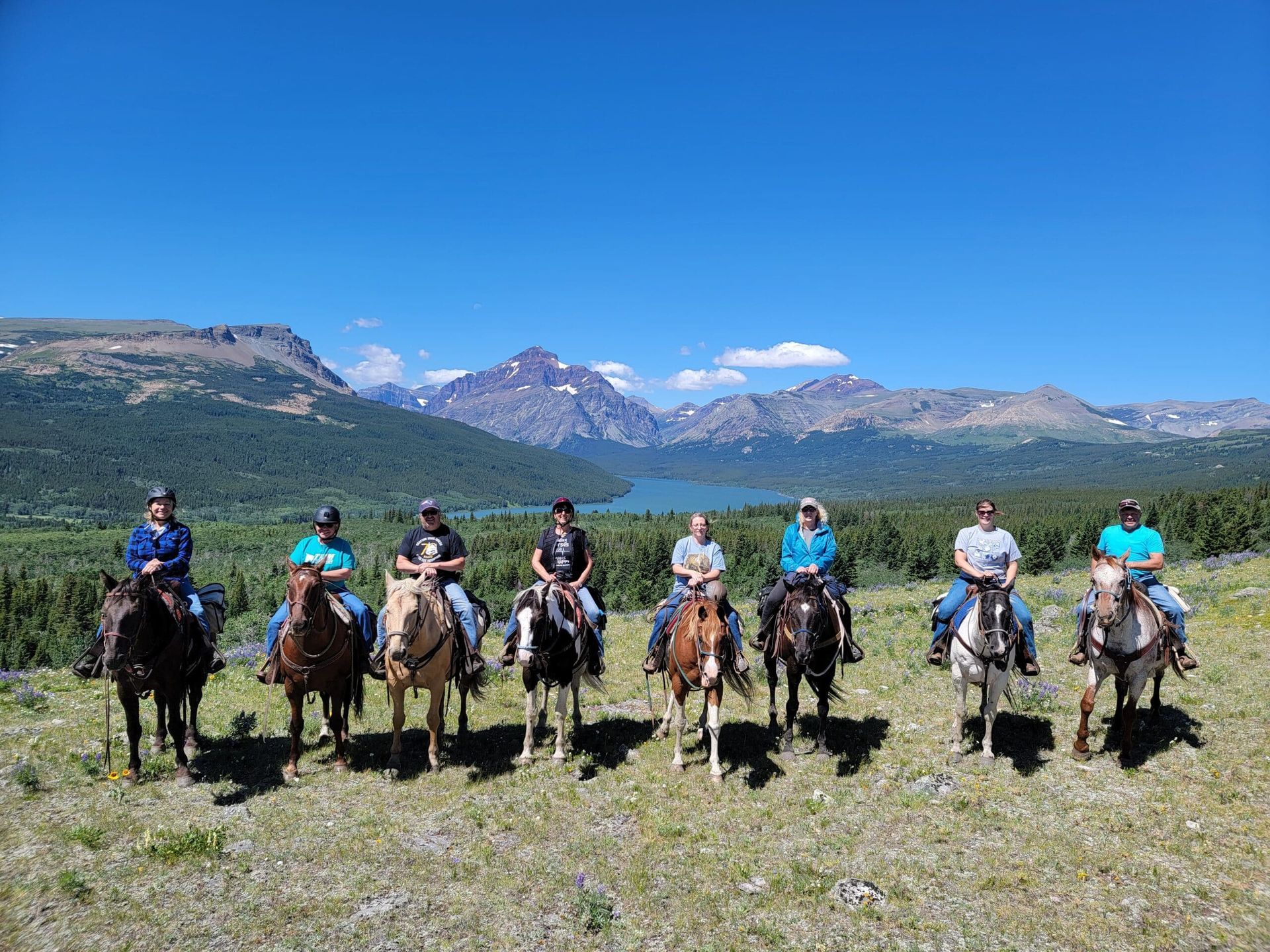 A group of people are riding horses in a field with mountains in the background.
