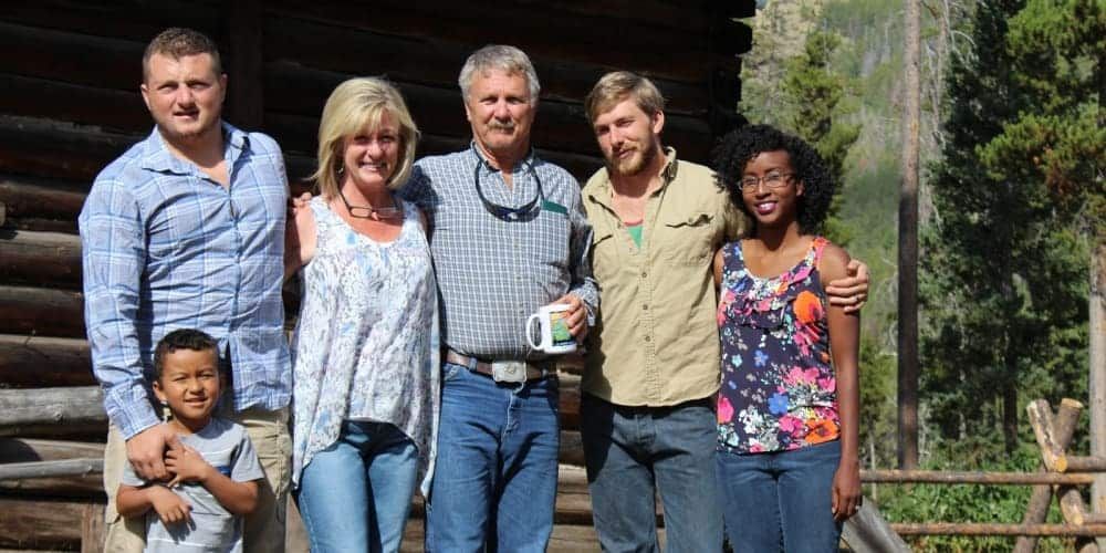 A family is posing for a picture in front of a log cabin.
