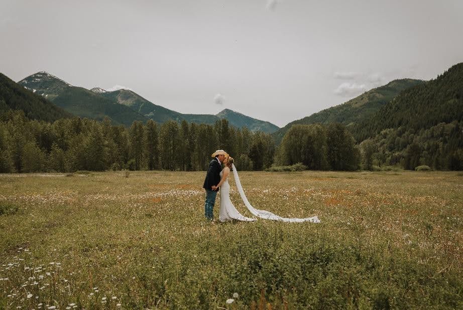 A bride and groom are kissing in a field with mountains in the background.