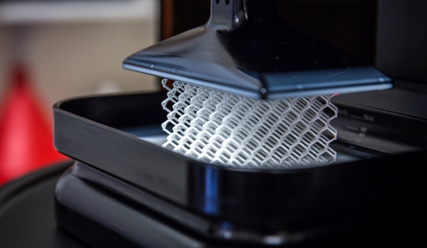Close-up of a 3D printer nozzle extruding white filament onto a black print bed