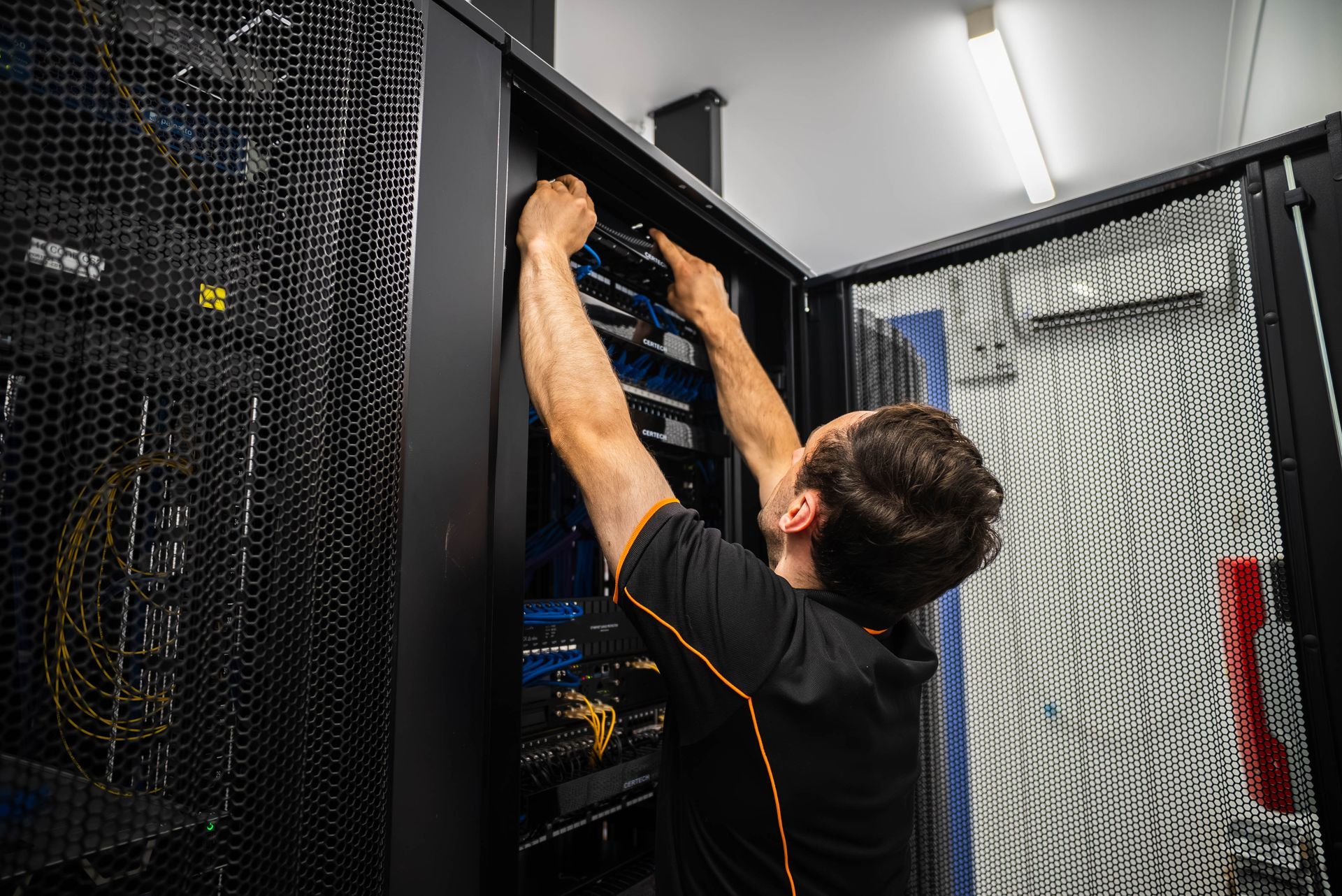 Technician working inside a server rack, reaching up to adjust cables in a data center.
