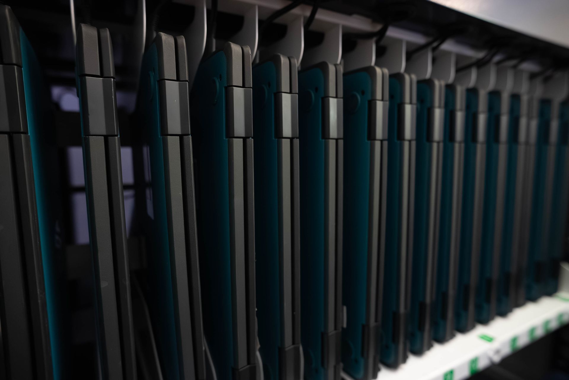 Row of black handheld devices docked on shelves in a dimly lit charging station