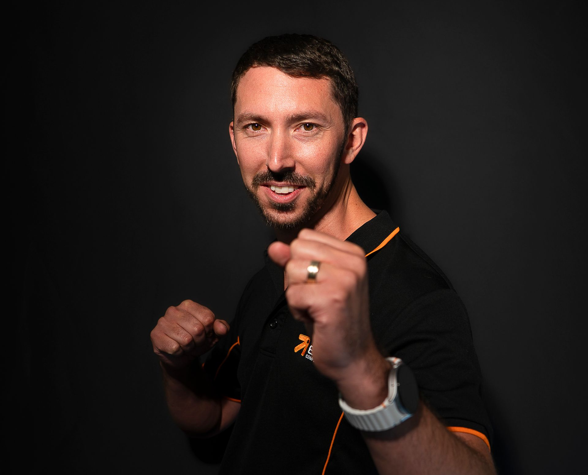 Man in black shirt with orange trim, fists raised in a boxing pose against a dark background