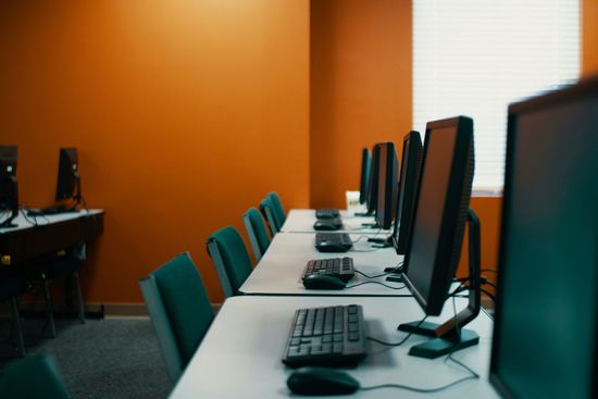 Empty computer lab with rows of monitors and keyboards against orange walls.
