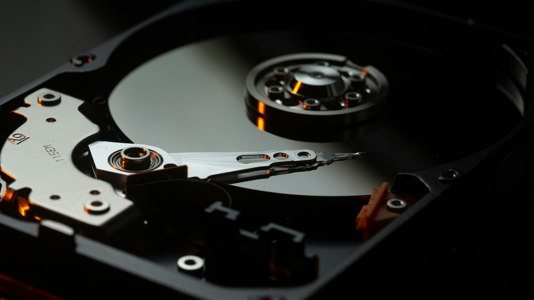 Close-up of an open hard drive platter and read arm in a dark setting
