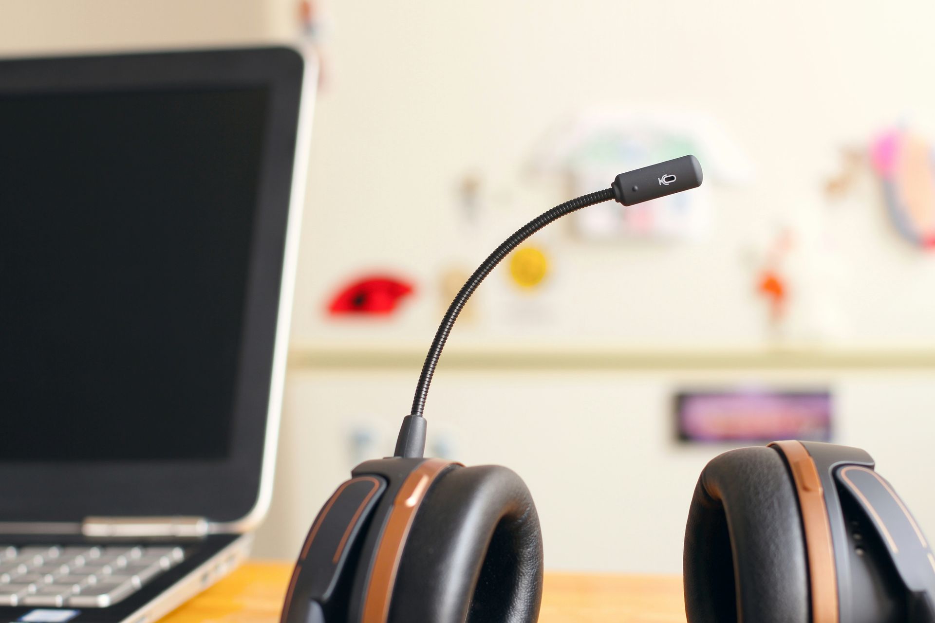 Black headphones with a microphone on a desk beside a laptop in a bright office setting