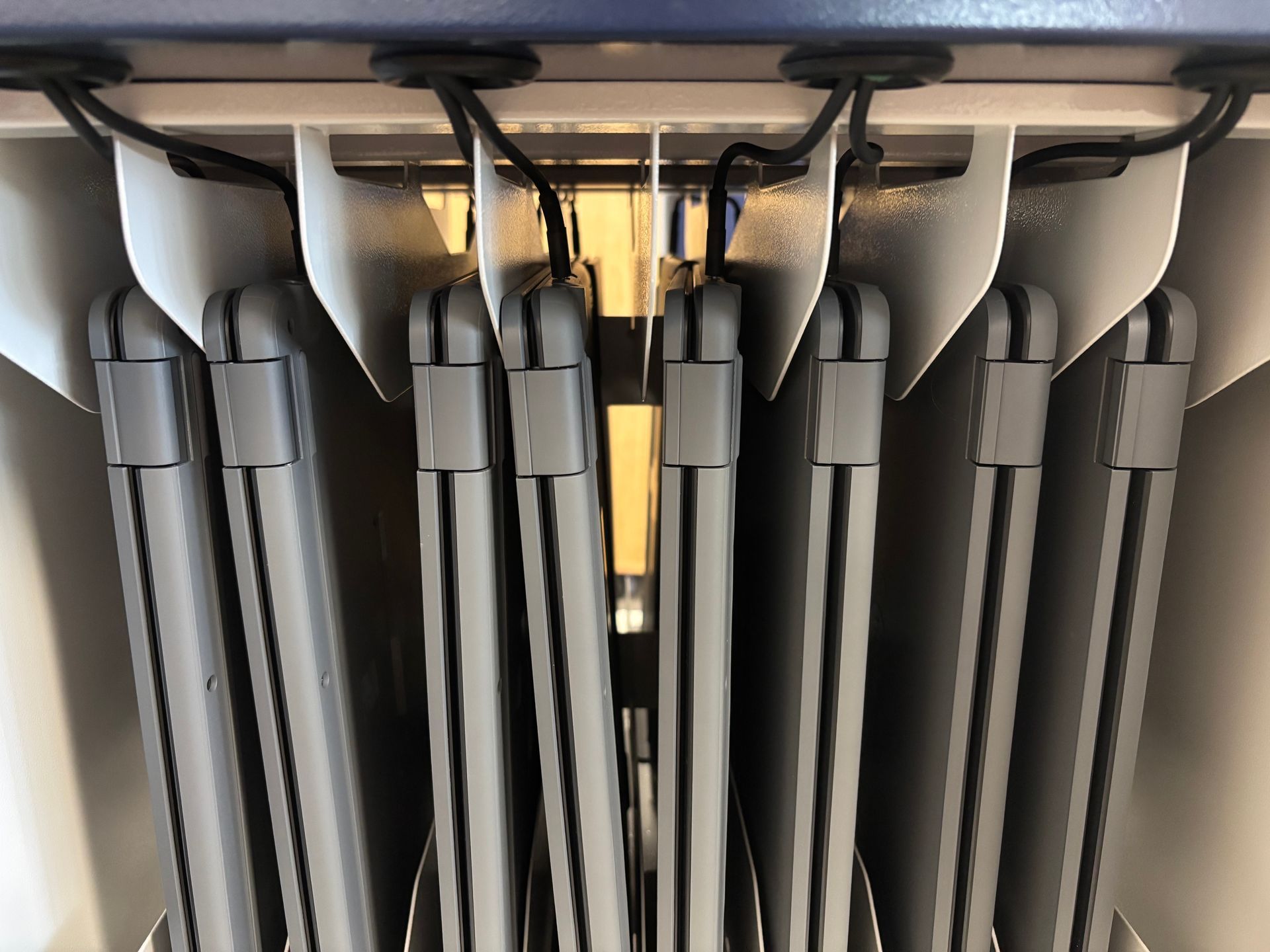Gray folding stools stacked tightly upright under a shelf, with black handles and metal supports visible.