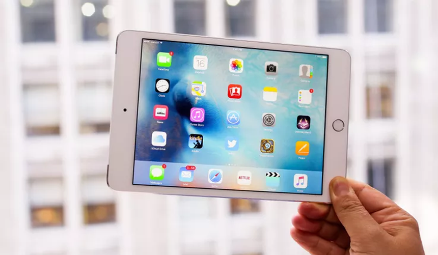Hand holding a white tablet showing a colorful app home screen indoors