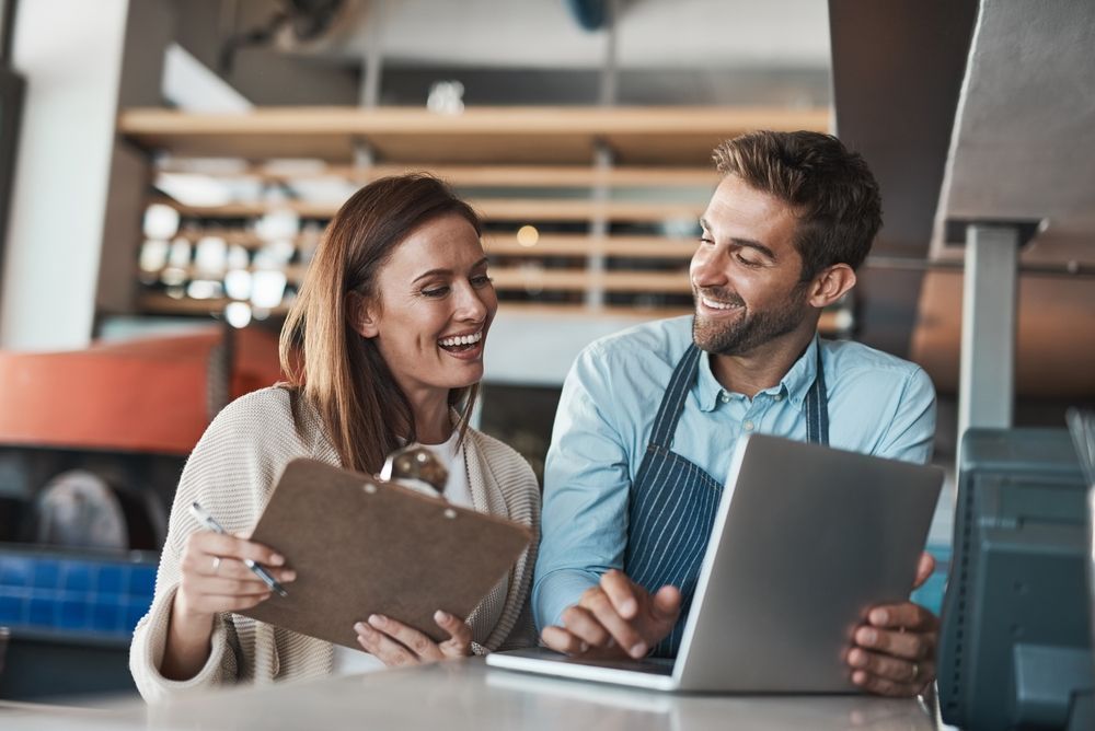 Two coworkers smiling and discussing a laptop at a table in a modern office