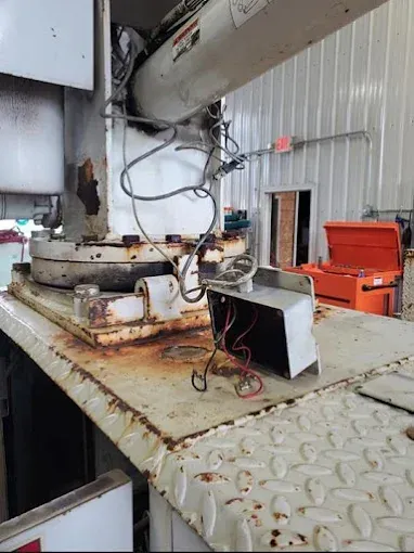 A disassembled electrical junction box with exposed red and black wires sits on a rusted industrial vehicle deck.