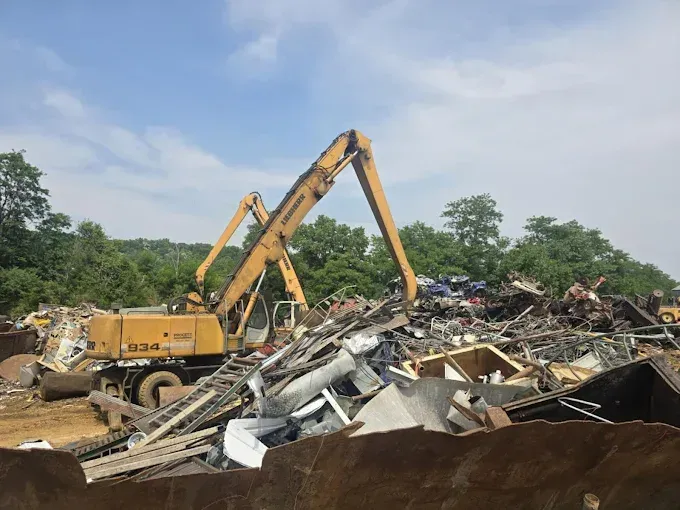 A yellow Liebherr excavator sorts through a large, chaotic pile of scrap metal in an industrial salvage yard.