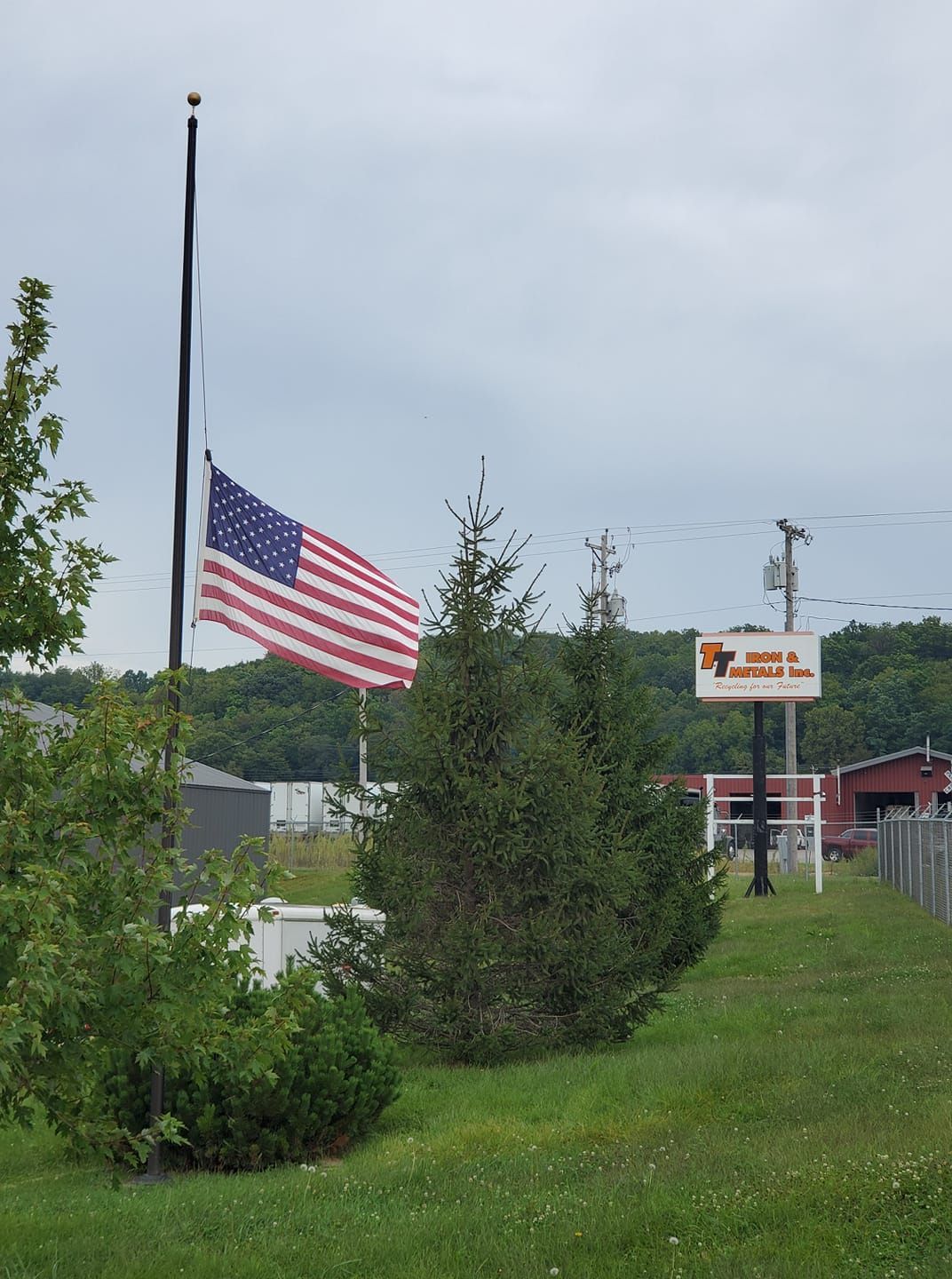 An American flag at half-staff on a pole in a grassy field next to a sign for 