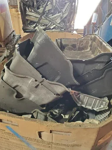 A cardboard bin filled with stacked, grey metallic automotive oil pans and scrap metal in a workshop.