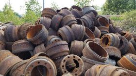 A large pile of rusted, used metal brake drums stacked outdoors.