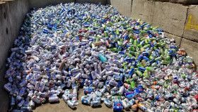 A large, high-angle view of a pile of crushed aluminum beverage cans in various colors stored within a concrete container.