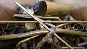 A box filled with assorted brass scrap metal, including pipes, tubes, and fittings.