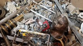 A cluttered pile of miscellaneous scrap metal pieces, including pipes, hardware, and a bronze-colored sphere.