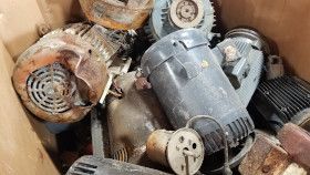 A cardboard box filled with several assorted, worn electric motors and industrial metal parts.
