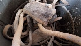 A collection of coiled, weathered, and dusty metal cables and heavy components inside a dark bucket.