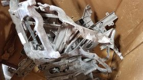 A pile of metallic, industrial-looking structural car parts or brackets stored inside a cardboard box.