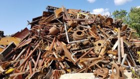 A large, towering heap of rusted metal scrap and industrial debris under a bright blue sky.