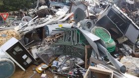 A large, chaotic pile of assorted scrap metal, discarded furniture, and household debris in an outdoor setting.