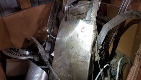 A cardboard box filled with various scraps of silver-colored metal components, including flat sheets and curved parts.