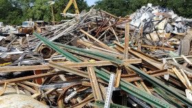 A large pile of assorted scrap metal, including rusted beams and green fence posts, at an outdoor salvage yard.