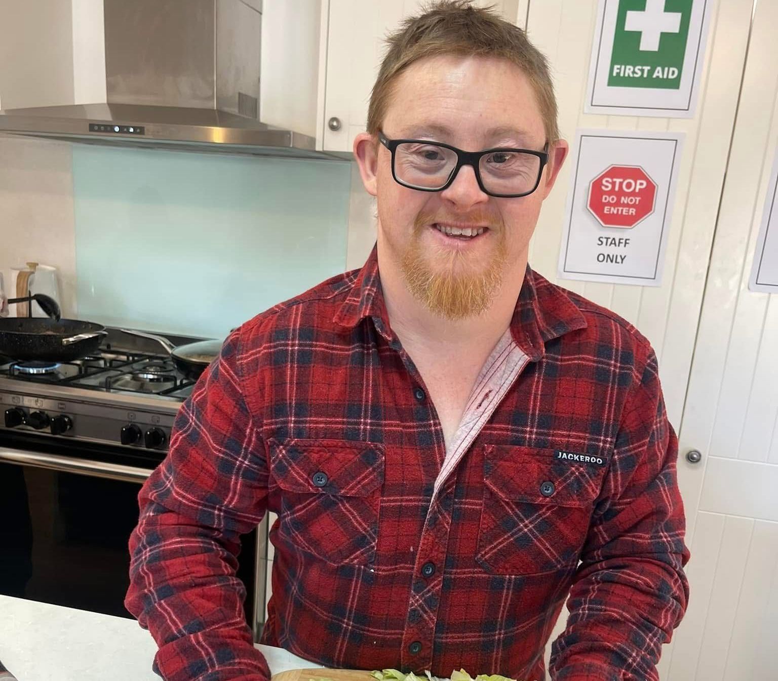 Skill building and daily activities. A man in a red plaid shirt is preparing food in a kitchen.