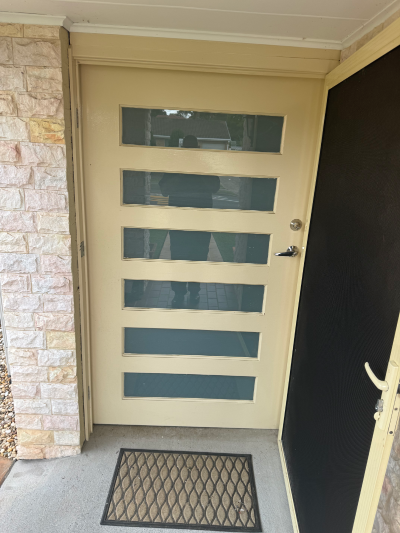 A widened door for accessibilty. A door with a mat in front of it and a brick wall behind it.