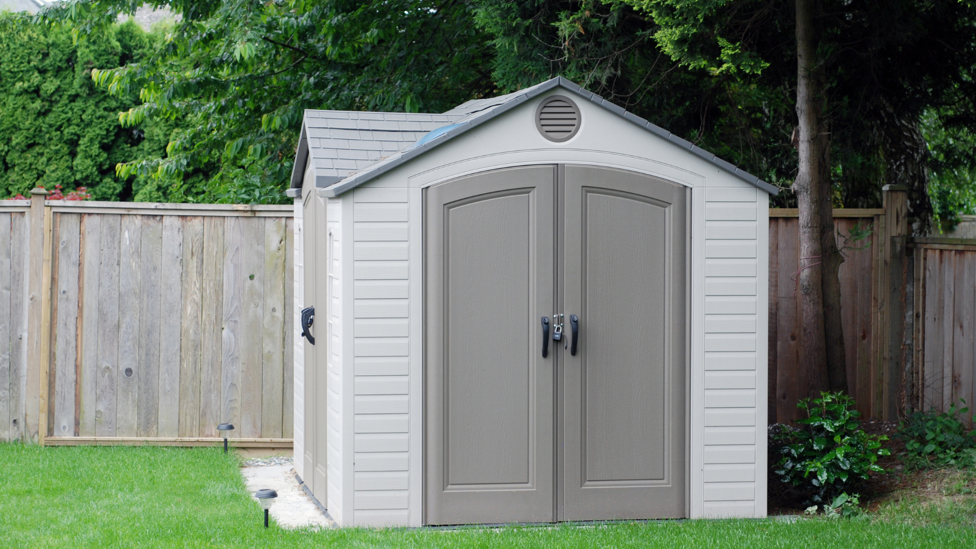 a shed is sitting in the middle of a lush green yard next to a wooden fence