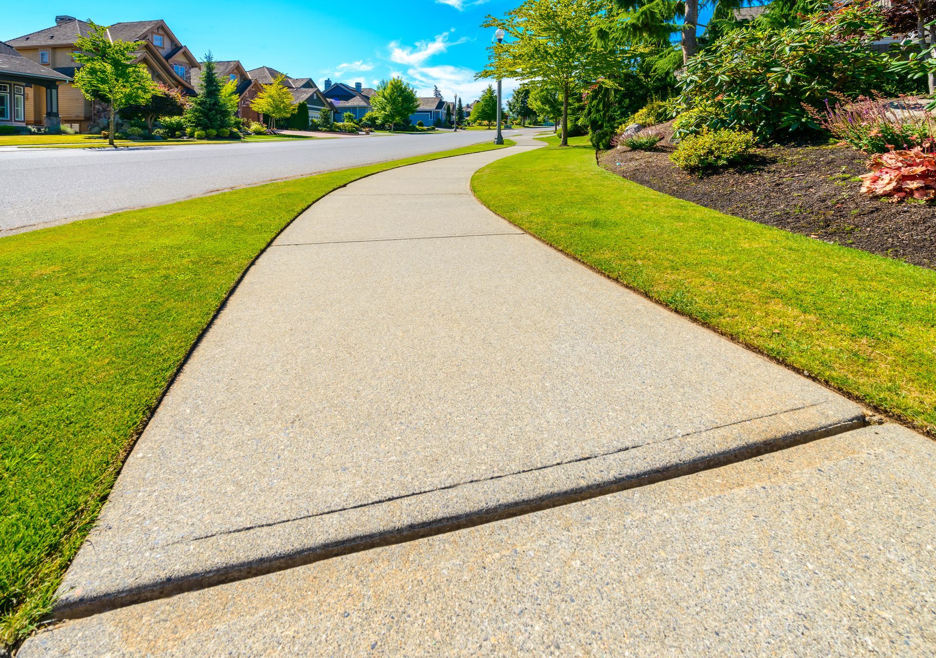 a concrete sidewalk in a residential neighborhood with a lush green lawn .