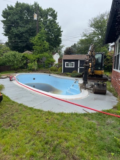 Backyard pool under construction beside a lawn, with an excavator and a small shed nearby.