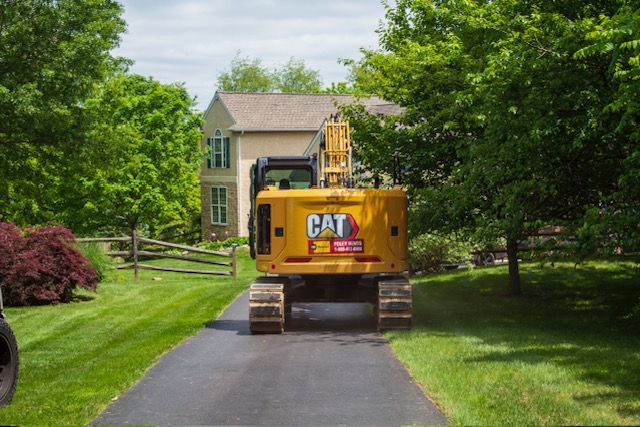 A gray stone walkway with a curved design, bordered by fresh dark mulch, leads alongside a house with a shaded porch.